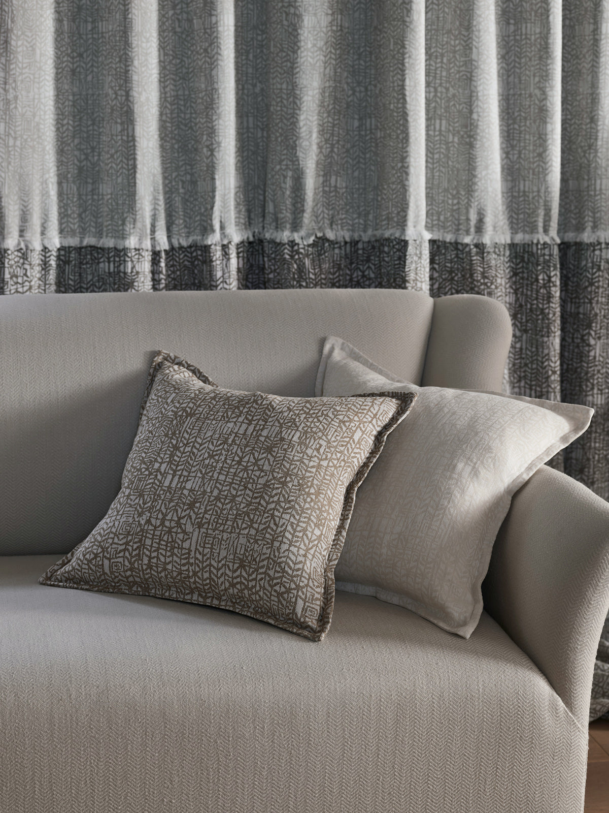 Gray sofa with textured pillows against a striped curtain background