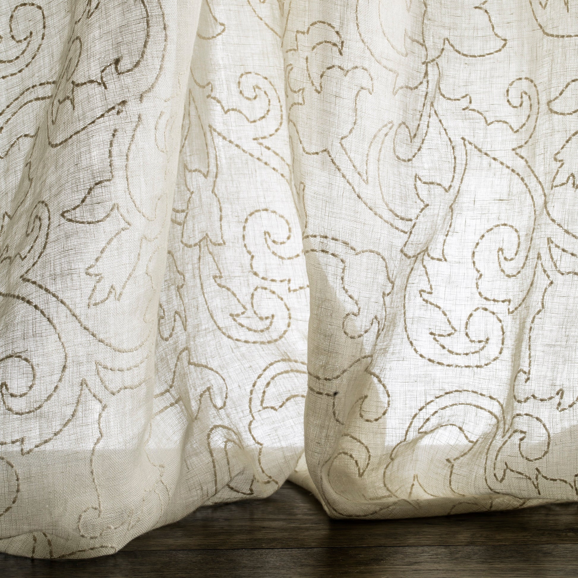 Sheer curtain with intricate floral pattern on a wooden surface