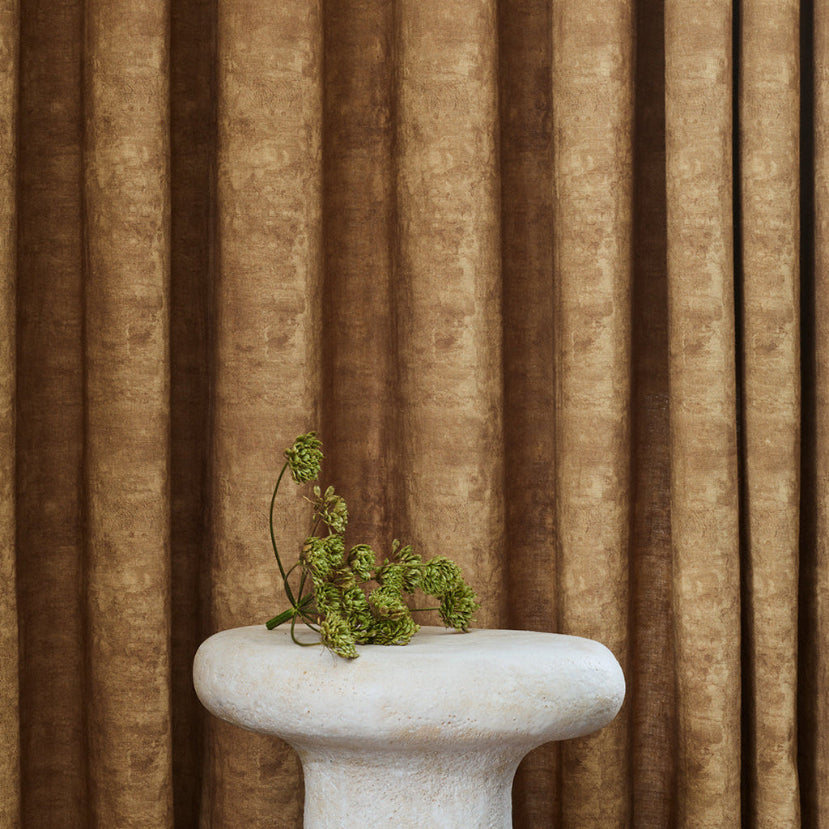 White pedestal with greenery against a brown curtain background