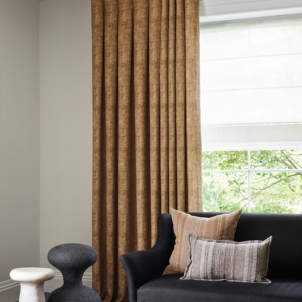 Living room with a dark gray sofa, decorative pillows, and a large window with brown curtains.